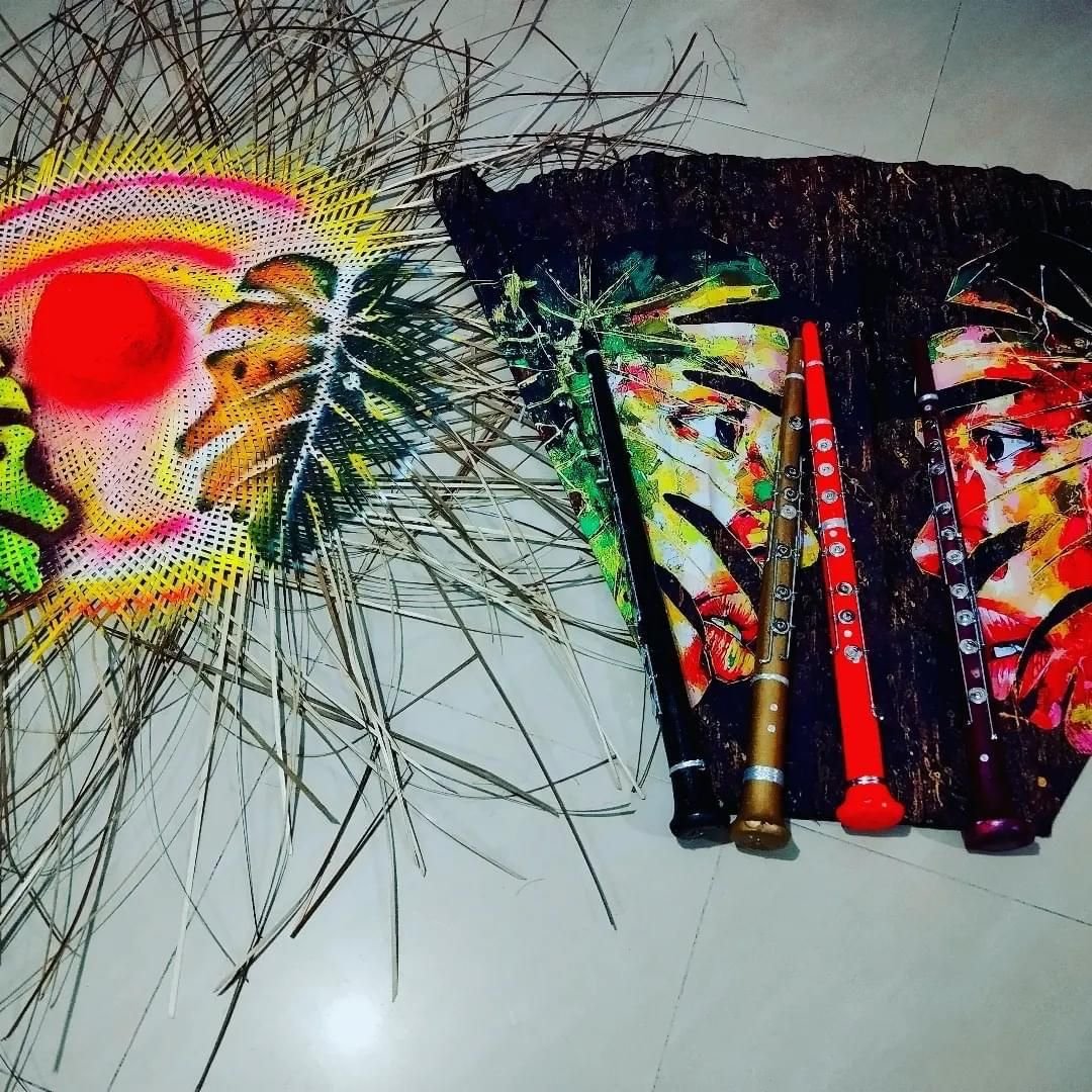 Sombrero tejido pintado en colores vivos junto a una tela estampada y cuatro flautas de colores.