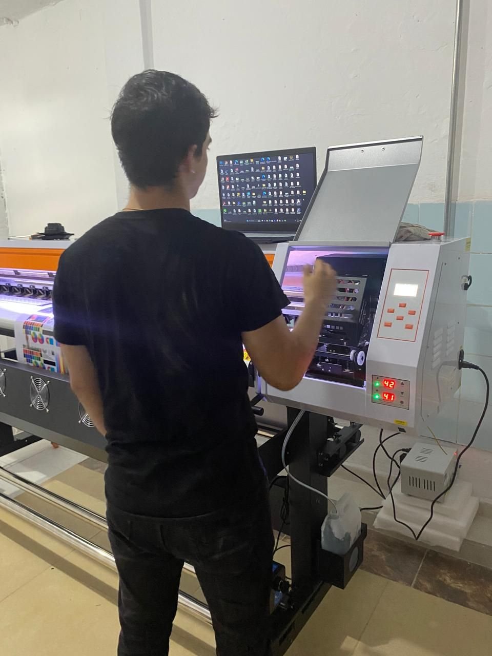 Persona operando una máquina de impresión de gran formato frente a un computador.